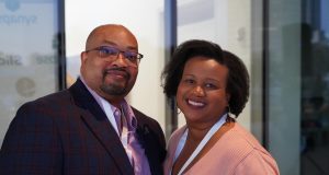 Ebony Vaz and Ronald Vaz in Synapse Summit Tampa 2023 wearing lanyards stand side by side indoors, smiling at the camera, representing their digital marketing agency.