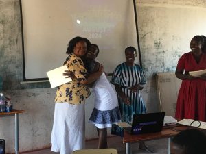Above Promotions in Zimbabwe; Two women from a digital marketing agency hug while holding a certificate in a classroom, with two other women standing nearby and a presentation projected on a whiteboard behind them.