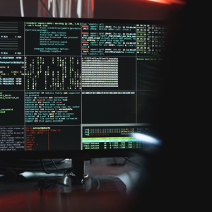 Computer screen displaying complex code and network data in a dimly lit room.