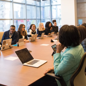 A group of people sitting around a conference table with laptops, engaged in a meeting inside a modern office space.