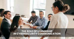 A group of professionals sitting around a table in a bright office, listening to a standing woman leading a discussion about leadership in AI and cybersecurity communication.