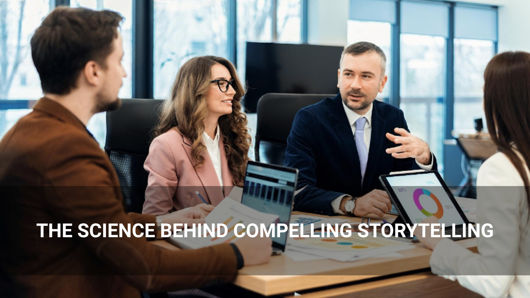 Four professionals in business attire sit at a conference table discussing charts and graphs, illustrating The Science Behind Compelling Storytelling with insightful data and visuals.