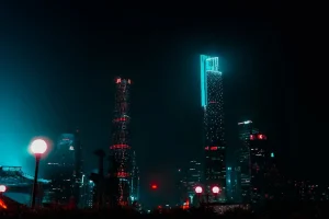 Night cityscape with illuminated skyscrapers and glowing streetlights, creating a futuristic atmosphere against a dark sky.