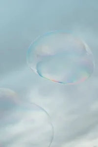 A close-up of two translucent soap bubbles floating against a light blue sky.