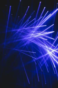 Blue laser lights crisscross in multiple directions against a dark background, creating a dynamic pattern.