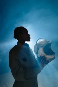 Silhouetted person in a uniform holding a space helmet against a blue, misty background.