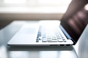 Side view of an open laptop on a reflective white surface with soft natural light streaming through a window in the background.